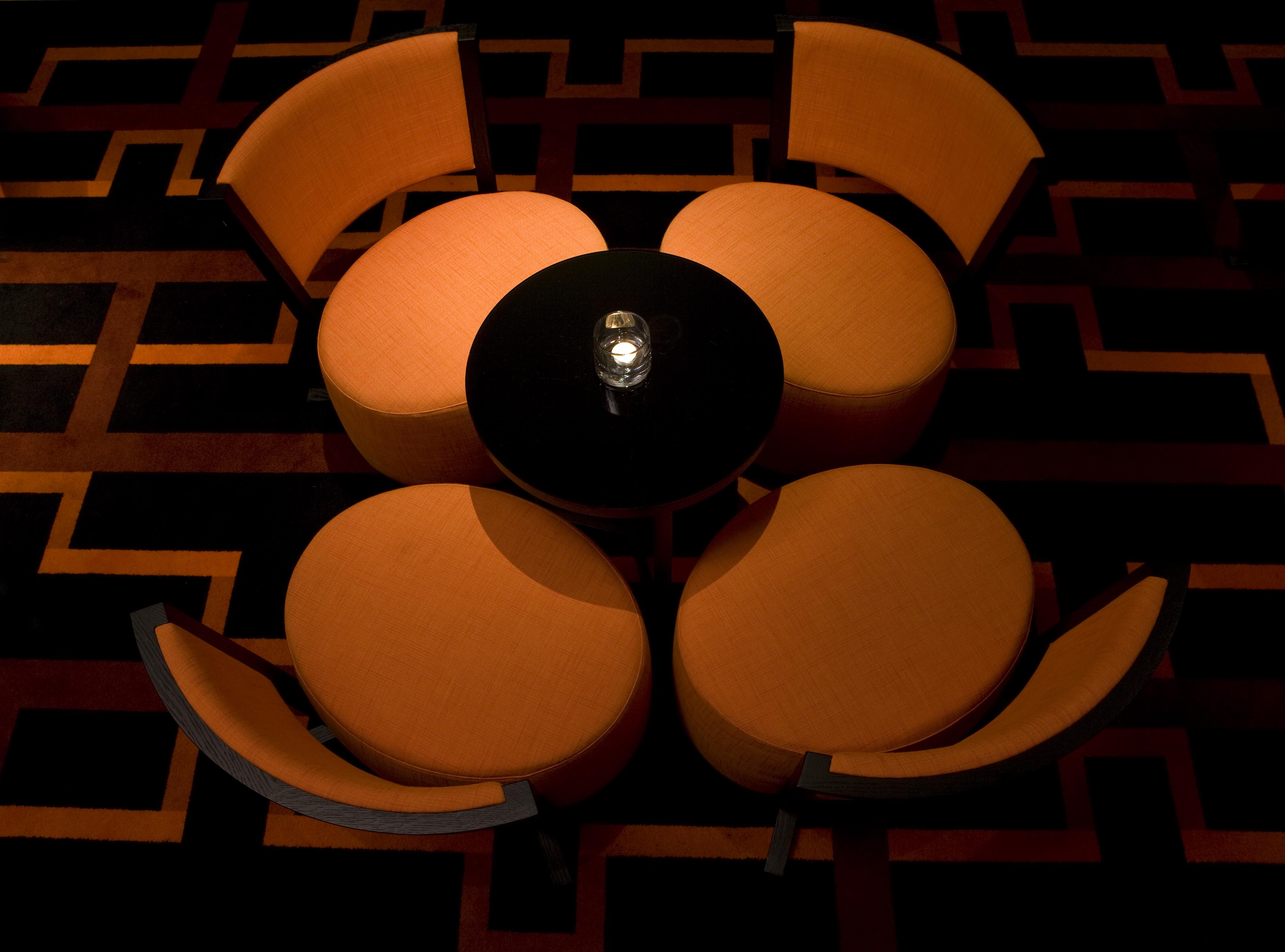 ザ フィッツウィリアム ホテル ベルファスト エクステリア 写真 The image shows a small seating arrangement consisting of four orange chairs arranged around a circular black table. The setting appears to be in a dimly lit area, emphasizing the warm tones of the chairs and the dark finish of the table. The floor d