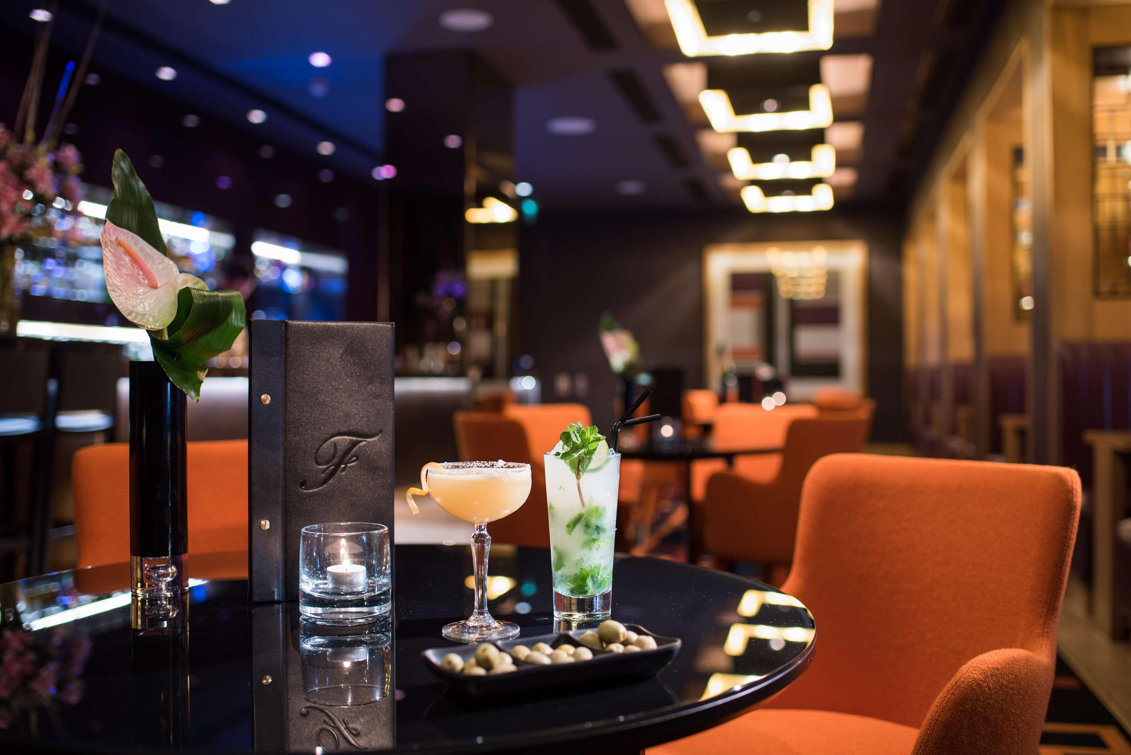 ザ フィッツウィリアム ホテル ベルファスト エクステリア 写真 The photo depicts a stylish bar or lounge setting. There are two cocktails on a black table: one appears to be a light-colored drink garnished with a slice of fruit, while the other is a green cocktail possibly containing mint. A small plate of olive