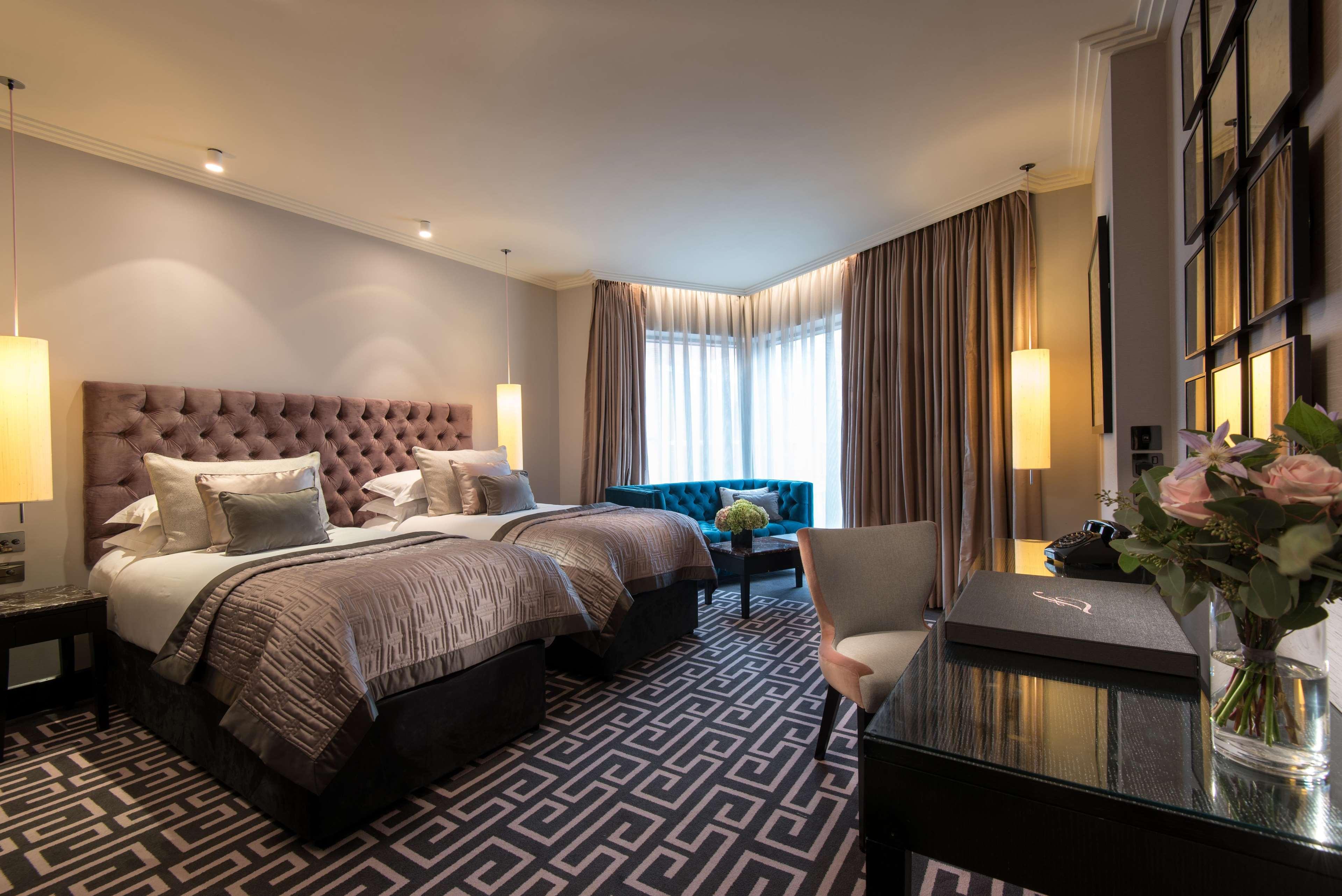 ザ フィッツウィリアム ホテル ベルファスト エクステリア 写真 The photo shows a stylish hotel room featuring two twin beds with tufted headboards and elegant bedding. On one side, there is a luxurious blue couch. Large windows are covered with light curtains, allowing natural light to enter. The floor is adorne