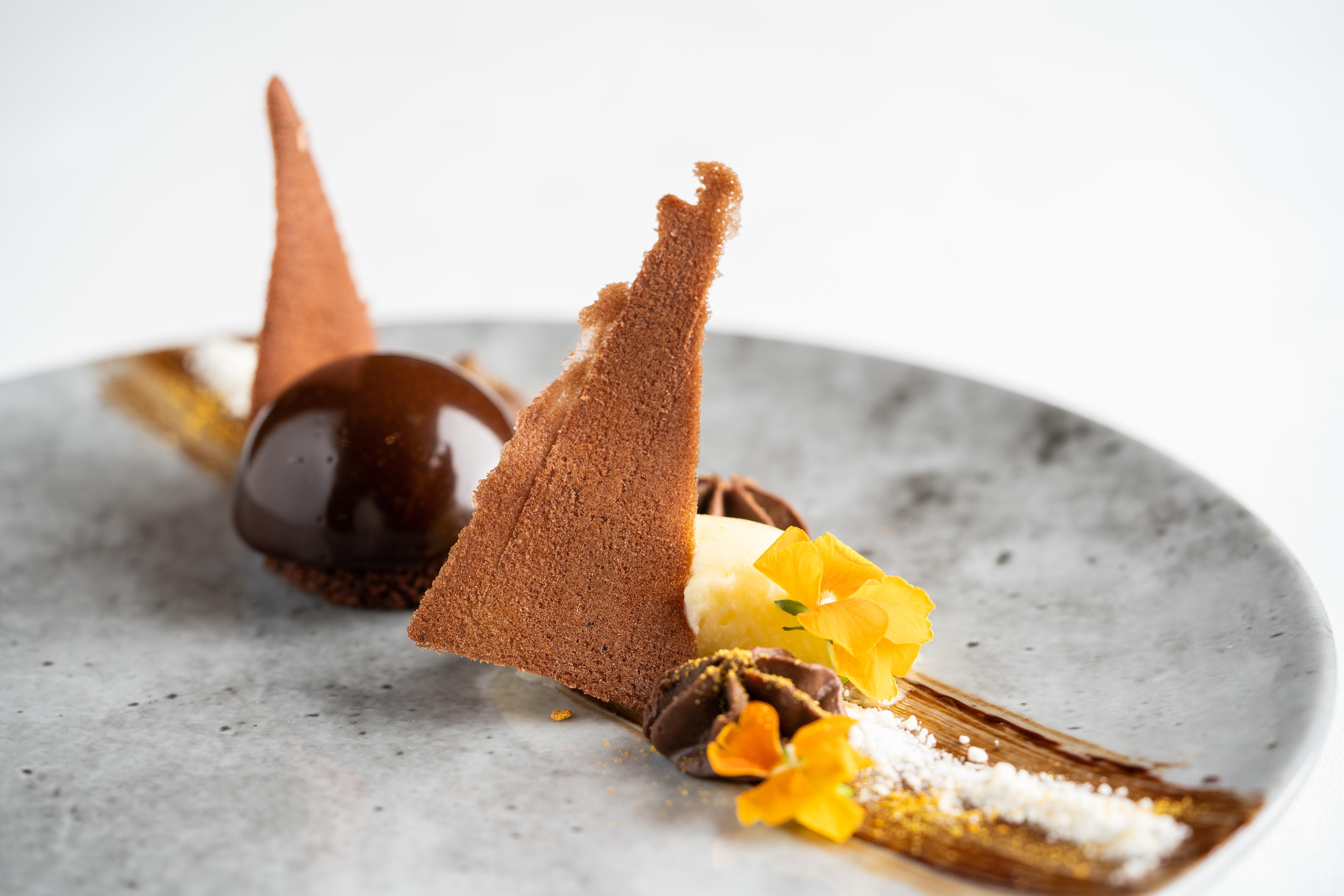 ザ フィッツウィリアム ホテル ベルファスト エクステリア 写真 The photo displays an artfully plated dessert. It features a glossy chocolate sphere, accompanied by various chocolate components, including triangular chocolate tuile pieces that resemble sails. The plate is adorned with delicate garnishes such as y