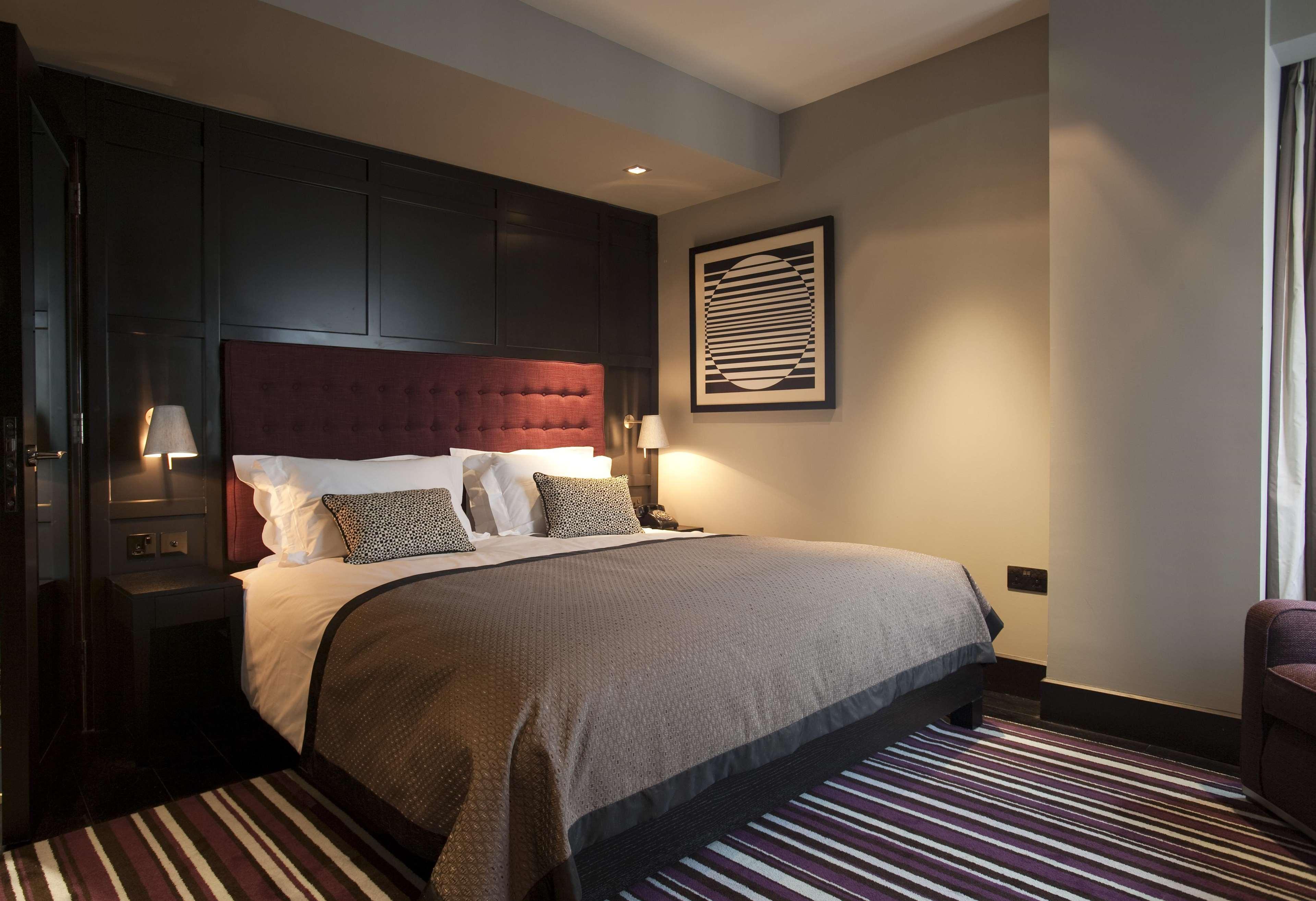 ザ フィッツウィリアム ホテル ベルファスト エクステリア 写真 The photo shows a stylish and modern hotel room. It features a large bed with a tufted headboard in a deep burgundy color. The bed is dressed with neutral-toned bedding and decorative pillows. On either side of the bed, there are small bedside lamps 